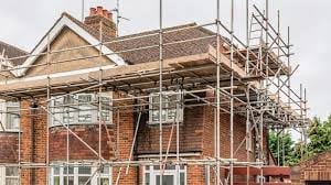 Red brick house under renovation with metal scaffolding covering the roof and upper section